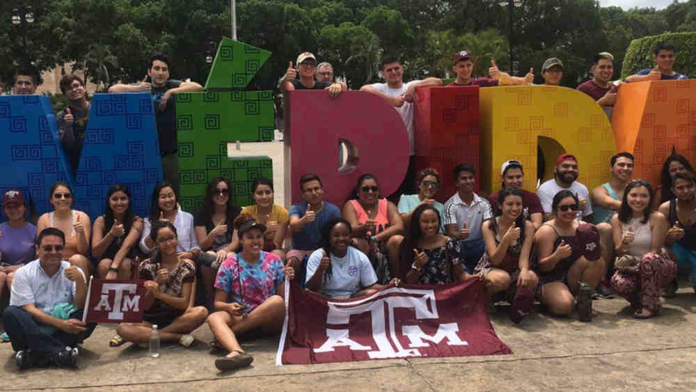学生们站在梅里达标志周围,前面是TAMU的旗帜