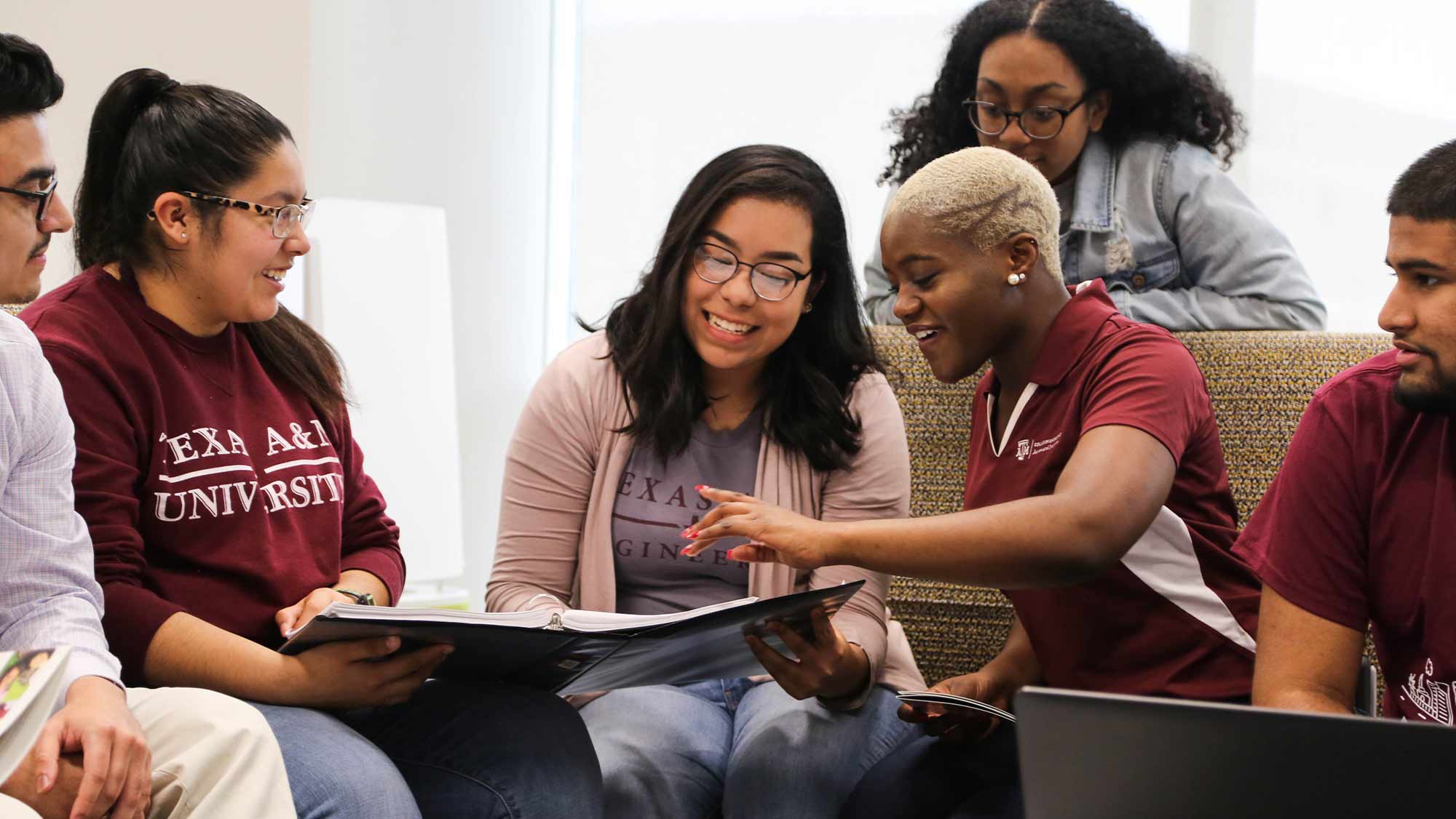 四个学生坐在沙发上，一个站在他们身后，一起看一个文件夹。