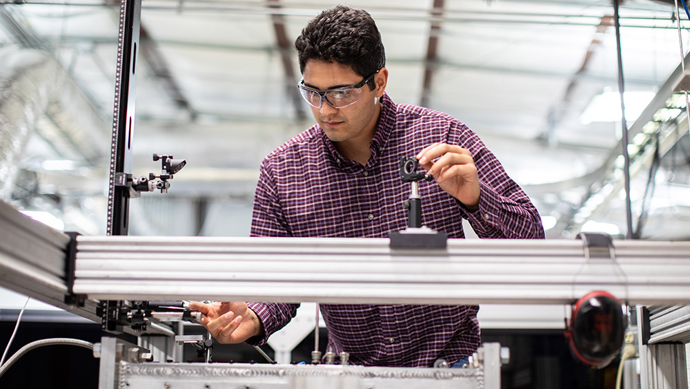 男学生戴着护目镜，在高超音速实验室里调试设备。