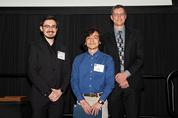 Two peer teachers standing on stage at awards banquet with Dr. Schaefer and smiling at the camera.