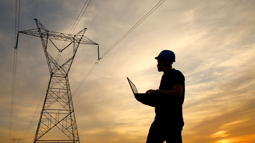 engineer working on a laptop near power lines