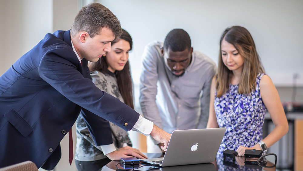 麦克唐纳博士在对4名学生讲话时指着笔记本电脑上的东西。
