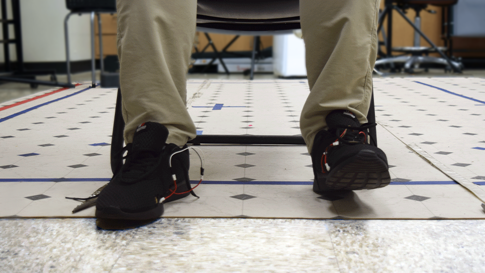 Seated person wearing shoes with sensors tapping their feet on the floor.