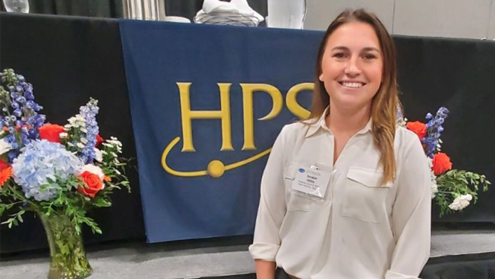 Jordan Hillis at the Health Physics Society meeting standing in front of their banner with the HPS logo.